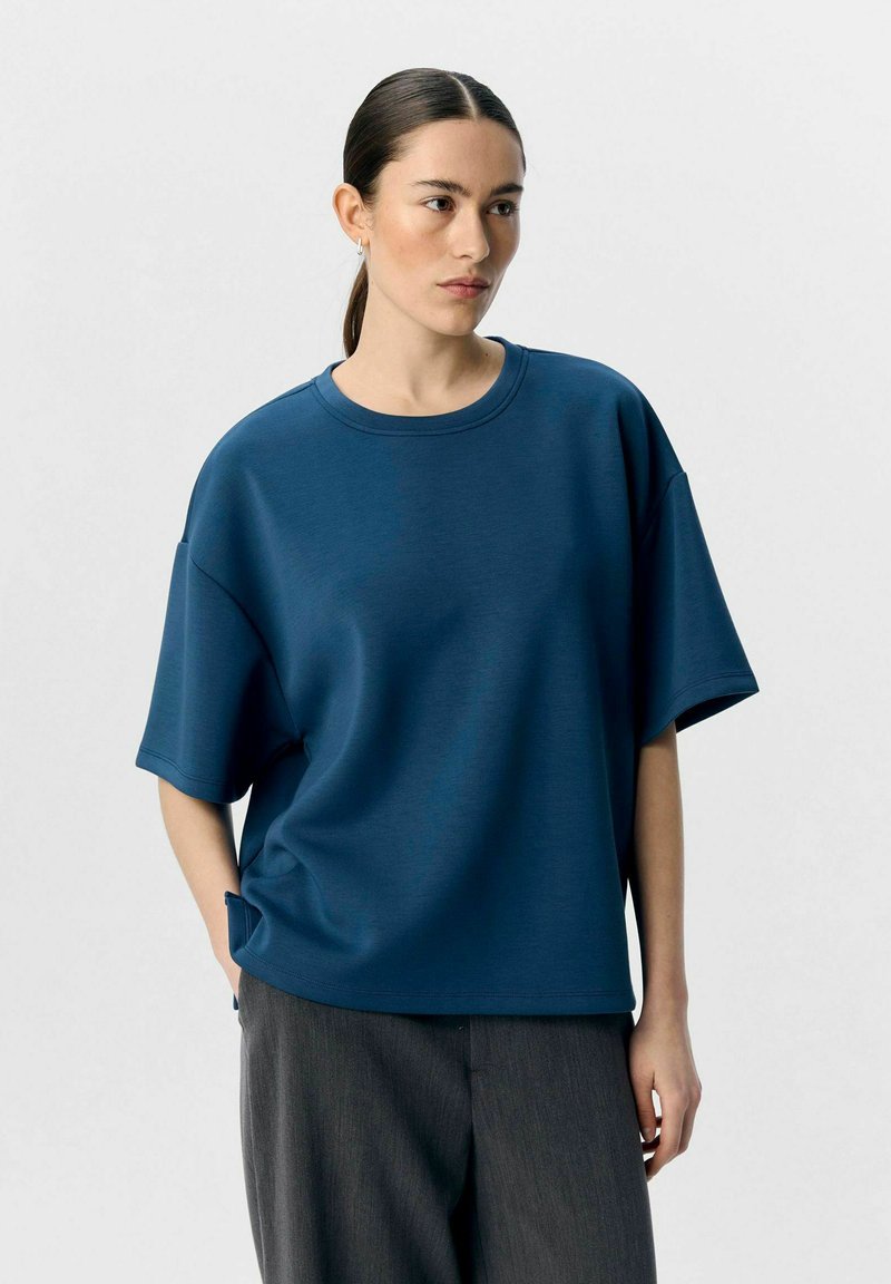 Overdimensioneret navy blå t-shirt i et glat stof med rund halsudskæring og korte ærmer, kombineret med teksturerede grå bukser.