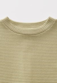 Tessuto beige a nido d'ape con scollatura rotonda, che mostra una texture e dettagli fini di righe orizzontali e verticali.