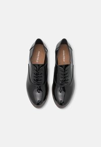 Scarpe in pelle verniciata nera con una texture liscia, punta affilata e design con laccetto. L'interno presenta una soletta marrone chiaro con il nome del marchio.