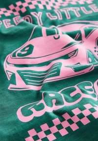 Roheline kangas, millel on roosa graafika autodest ja tekst "Kiire Pisike Võidusõitja" koos ruuduliste mustrite aktsentidega. Sile tekstuur.