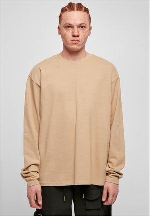 Cămașă bej cu mânecă lungă, cu o croială lejeră, guler rotund și umeri căzuți. Textură moale, design minimalist, fără modele sau accente vizibile.