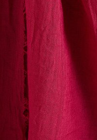 Tissu rouge texturé avec un tissage lâche, présentant des bords effilochés. La surface est légèrement inégale, accentuant sa sensation naturelle.