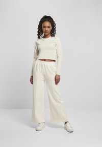 Kerman pitkähihaine crop-top yhdistettynä leveälahkeisiin kermanvärisiin housuihin. Housuissa on näkyvät saumat. Kenkinä valkoiset tennarit.
