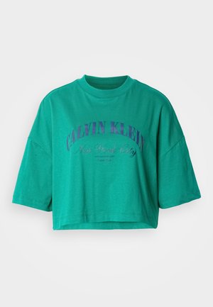 Kurzes T-Shirt in Petrol mit rundem Ausschnitt und lila Schriftzug "Calvin Klein New York City" auf der Vorderseite.