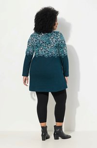 Tummansininen tunika, jossa on kukka-ompelu selkäpuolella, pitkät hihat, yhdistetty mustiin legginsseihin ja nilkkabootseihin, sileä rakenne ja istuva malli.