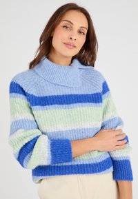 Maglione a righe blu e verdi con colletto alto a coste. Texture morbida. Presenta maniche ampie e un design corto.