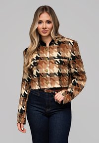 Beskåret jakke med et brunt, sort og cremefarvet ternet mønster, guldknapper og sort krave. Bæres over mørkeblå jeans.