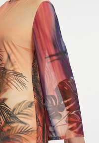 T-shirt à manches longues dégradé de pêche à violet, avec un motif de feuille de palmier et un tissu transparent sur les manches. Texture lisse sur l'ensemble.