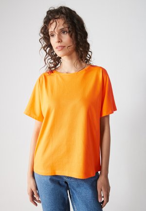 Oranjekleurig katoen T-shirt met korte mouwen en een ronde halslijn, gecombineerd met blauwe denim jeans. De stof lijkt glad en lichtgewicht.