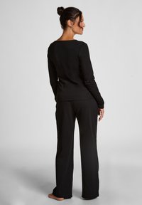 Zwarte langemouwen top met een vierkante halslijn, gecombineerd met bijpassende zwarte broeken. De stof lijkt zacht en rekbaar met een ontspannen pasvorm.