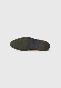 Suela de zapato de cuero marrón con un fondo de goma verde texturizada, que presenta un patrón hexagonal y un acento azul contrastante cerca del talón.