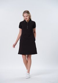 Robe polo noire à manches courtes, en tissu texturé, avec des accents blancs sur le col. Dotée d'une fermeture par boutons et de poches latérales.