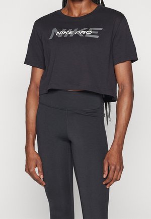 Persoon draagt een zwart cropped Nike Pro T-shirt en zwarte leggings met hoge taille tegen een effen achtergrond.