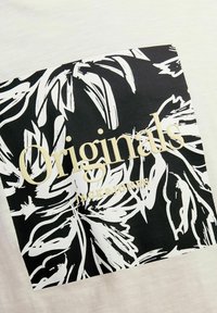 Bijela majica s crno-bijelim uzorkom lišća na kvadratnom grafičkom izdanju; zlatni tekst "Originals" i logo "Jack & Jones".