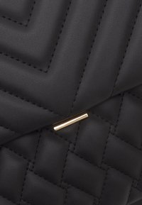 Czarna pikowana skórzana kopertówka z wypukłym wzorem w zygzak i złotym zapięciem. Teksturowana powierzchnia z widocznym ściegiem.