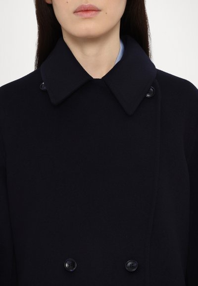 Cappotto in lana di un blu scuro, caratterizzato da un design doppiopetto, ampio colletto e grandi bottoni neri. Texture liscia con una vestibilità su misura.