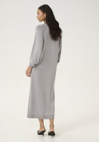 Robe tricotée grise avec de longues manches bouffantes, longueur mi-mollet, dotée d'un léger scintillement, d'un ourlet côtelé et d'une silhouette décontractée. Chaussures à talon noires.
