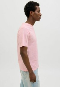 Roze T-shirt met korte mouwen, gemaakt van katoen, met een normale pasvorm en ronde hals. Gecombineerd met lichtblauwe denim jeans. Zijkant weergegeven.