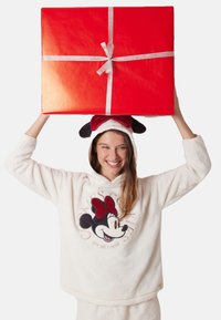Rød gaveæske med sølvsløjfe holdt over en person iført en hvid fleece hoodie med et Minnie Mouse-design og en matchende hat med ører.