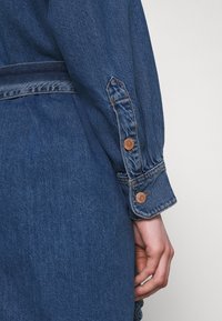 Mörkblå denimjacka med knappmanschetter, en strukturerad design och synliga söm detaljer. Slät textur med en klassisk finish.