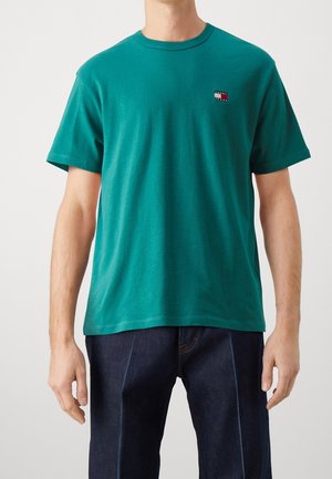 Kurzärmliges T-Shirt aus teal-farbenem Baumwollstoff mit einem kleinen Logopatch auf der Brust. Normale Passform mit Rundhalsausschnitt und glatter Textur.