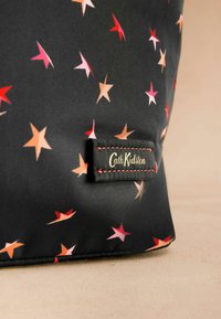 Geantă neagră cu un model de stele în roșu, roz și bej. Are o etichetă cusută pe care scrie "Cath Kidston." Textură netedă.