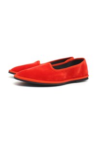 Pantofole rosse in suede con punta affusolata, suola nera piatta e design minimalista. Texture liscia con un bordo arancione a contrasto.