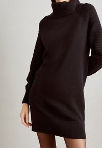 Robe-pull en tricot marron foncé avec un col montant, des manches texturées et un ourlet côtelé. Présente une coupe décontractée et une longueur moyenne.