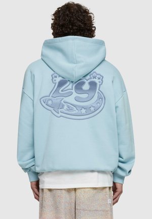 Ljusblå hoodie med en stor broderad design som visar "29", en raket och stjärnor på baksidan. Mjukt tyg med en avslappnad passform.