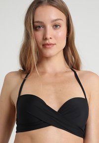 Čierny bikiny top s dizajnom prekríženia, vyrobený z hladkej látky. Obsahuje tenké nastaviteľné ramienka a štruktúrovaný, vypchávkovaný dekolt.