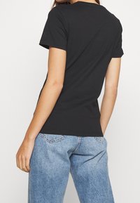 Czarna, dopasowana koszulka z krótkim rękawem, wykonana z miękkiej bawełny, z okrągłym dekoltem. Noszona z jasnoniebieskimi, luźnymi dżinsami.