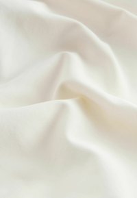 Tissu blanc avec une texture lisse et douce, présentant de subtils plis et ondulations. Le matériau semble léger et tombe délicatement.