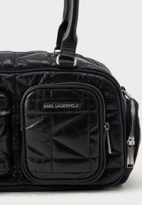 Černá prešívaná kožená taška přes rameno s výrazným logem, zipovými kapsami a hladkým povrchem. Strukturovaný tvar s dvojitými uchy.