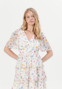 Robe à imprimé floral en tissu léger ; présente un décolleté en V, des manches courtes à volants et des volants en couches avec un mélange de fleurs colorées.