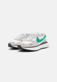 Zapatillas Nike que presentan una combinación de ante gris y textil blanco, con detalles en verde y una suela de goma negra, diseñadas con una silueta moderna.