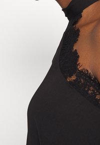 Svart ärmlös topp med spetsdetalj längs halsringningen, med en mjuk textur och halterneck-design.