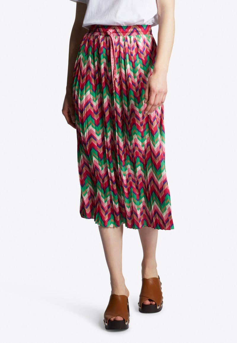 Jupe plissée à motif chevron multicolore avec taille smockée et ceinture assortie, associée à des chaussures en bois à plateforme ouvertes et marron.