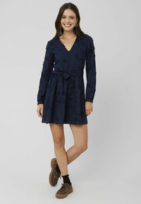 Robe bleu marine avec des manches longues, décolleté en V, et broderie florale. Présente une jupe à volants et une ceinture nouée pour un ajustement ajustable.