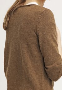 Maglione lavorato a maglia marrone con maniche lunghe, scollo rotondo e una consistenza morbida. Mostra il retro con dettagli a coste sottili.