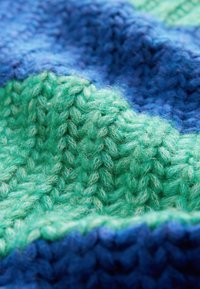 Gebreide stof in tinten blauw en groen, met gestructureerde patronen van zachte, pluizige vezels en diverse breistijlen.