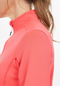 Helles Koralle-Pullover mit hohem Kragen, strukturiertem Stoff und halbem Reißverschluss vorne. Verfügt über minimalistische Nähte und ein kleines Logo-Detail.