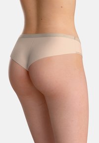 Beige hipsterunderkläder med en slät textur och ett brett, ljusgrått midjeband med en subtil logotyp; designade för komfort och passform.