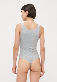 Grauer Baumwoll-Tank-Body mit ärmellosem Design, Rundrücken und String-Schnitt. Glatte Textur und taillierte Form, ideal zum Schichten.
