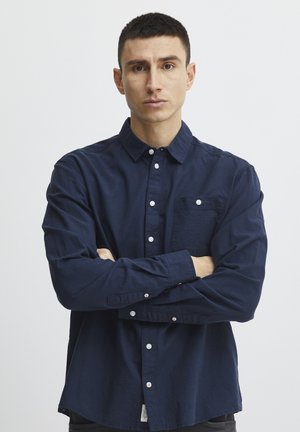 Navy blue button-up shirt with long sleeves, a chest pocket, and white buttons. The fabric appears textured and lightweight.