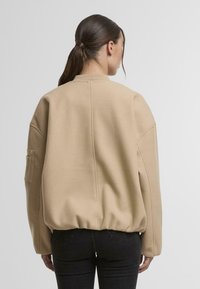 Beige oversized mikina s texturovaným povrchem, žebrovaným límcem a elastickým lemem. Má boční kapsu a spadlými rameny.