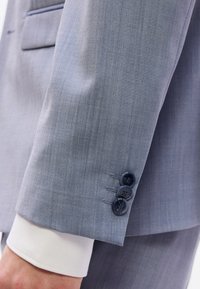 Μανίκι από ανοιχτό μπλε σακάκι με ομαλή υφή υφάσματος, τρία σκούρα μπλε κουμπιά και μανικέτι λευκού πουκάμισου από κάτω.