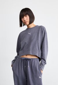 Sudadera gris corta con un cuello redondo y puños acanalados, que presenta un logo blanco de Puma. Combinada con pantalones jogger grises con cordón a juego.
