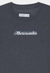 Felpa grigia scura con scollo rotondo, con il logo bianco in corsivo "Abercrombie" sul davanti. L'etichetta indica la taglia 9/10, prodotta in Vietnam.