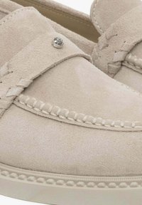 Suede loafers in light beige with stitched accents, a decorative strap, and silver hardware detail on the front. Soft texture and rounded shape.