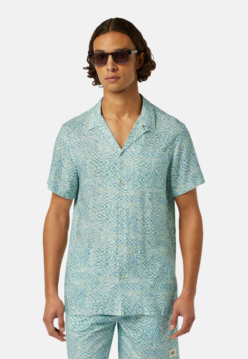 Korte mouwen, geknoopte blouse in lichtblauw met een geometrisch patroon. Gemaakt van zachte stof, het heeft een losse pasvorm en witte knopen.